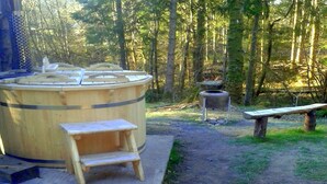 Estructura de sauna de madera con banco y escalones, rodeada de un área boscosa.