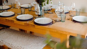 Une table de salle à manger en bois, mise avec des assiettes, des verres et un vase rempli de fleurs.