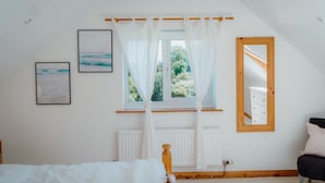 Une chambre à coucher avec un lit, une fenêtre ornée de rideaux légers, une tête de lit en bois, un miroir et deux tableaux encadrés accrochés au mur.