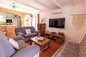 A living room with a sofa, a coffee table, and a TV. There is a kitchen visible in the background.