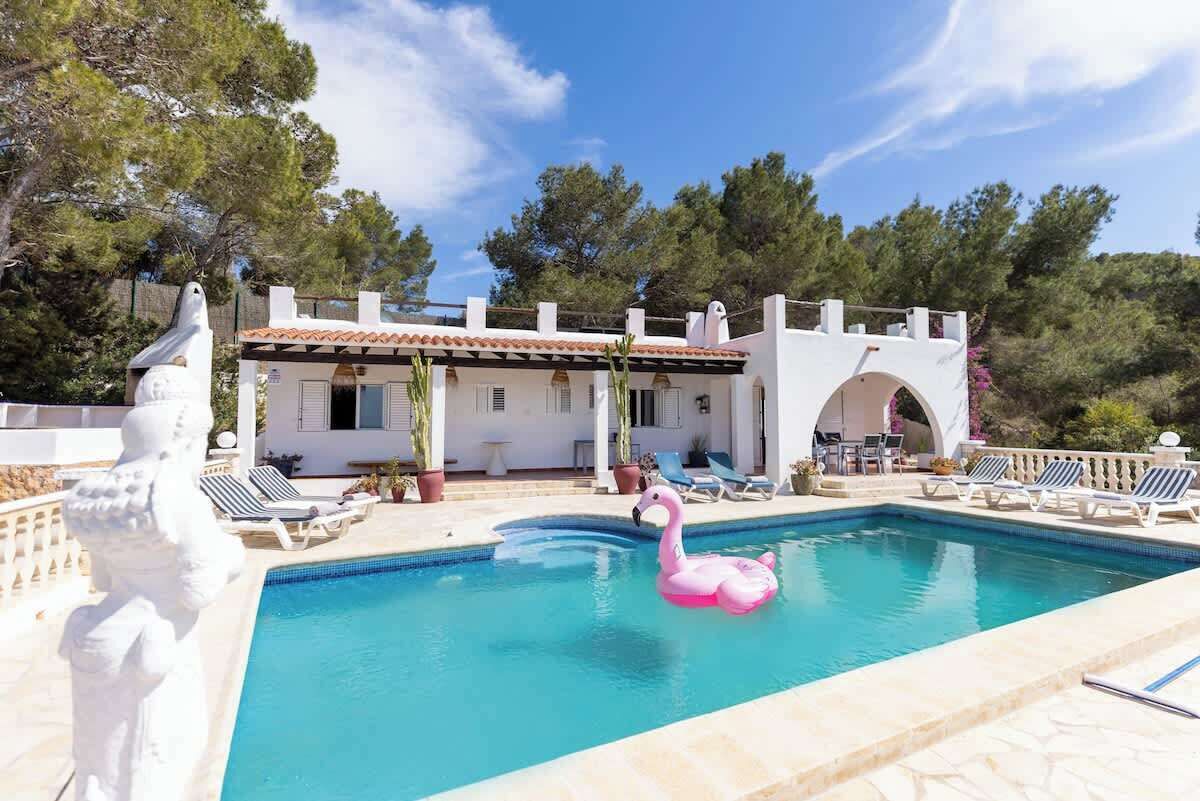 Una piscina con un gonfiabile a forma di fenicottero rosa, sedie a sdraio e un edificio bianco con tetto in tegole.