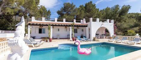 Una piscina con un gonfiabile a forma di fenicottero rosa, sedie a sdraio e un edificio bianco con tetto in tegole.