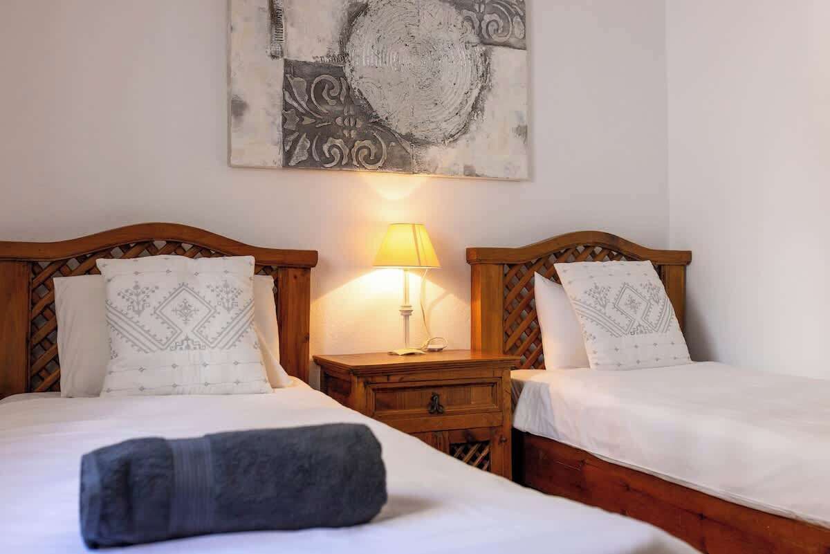 Une chambre d’hôtel avec deux lits en bois, chacun agrémenté d’oreillers à motifs et d’une table de chevet avec une lampe.