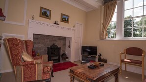 A living room with a fireplace, a television, a wooden coffee table, and two armchairs.