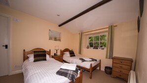 A bedroom with two single beds, a wooden dresser, a window with curtains, and a mirror on the wall.