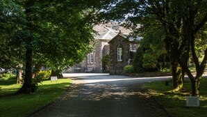 A pathway leading to a stone building with a traditional architectural style, surrounded by lush greenery and trees.