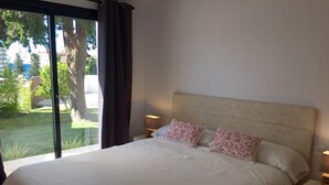 A bedroom with a large bed, two bedside tables, and a view of a garden through a sliding door. - 4 Beds & 4 Bath, 150mts from the beach, Private Heated Pool, BBQ (Fuengirola)