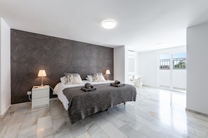 Une chambre à coucher moderne avec un grand lit, deux lampes de chevet, un mur d’accent de couleur foncée et une grande fenêtre.