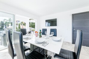 Un coin repas avec une table blanche, des chaises noires et un téléviseur à écran plat fixé au mur.