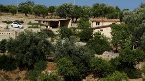 A rural house with a car parked outside, surrounded by trees and a clear sky.