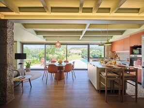 A modern kitchen with a large island, dining area with round table and chairs, and a view of the outdoors. - Private Riverside Hideaway | Infinity Pool & Kayak (Maureles)
