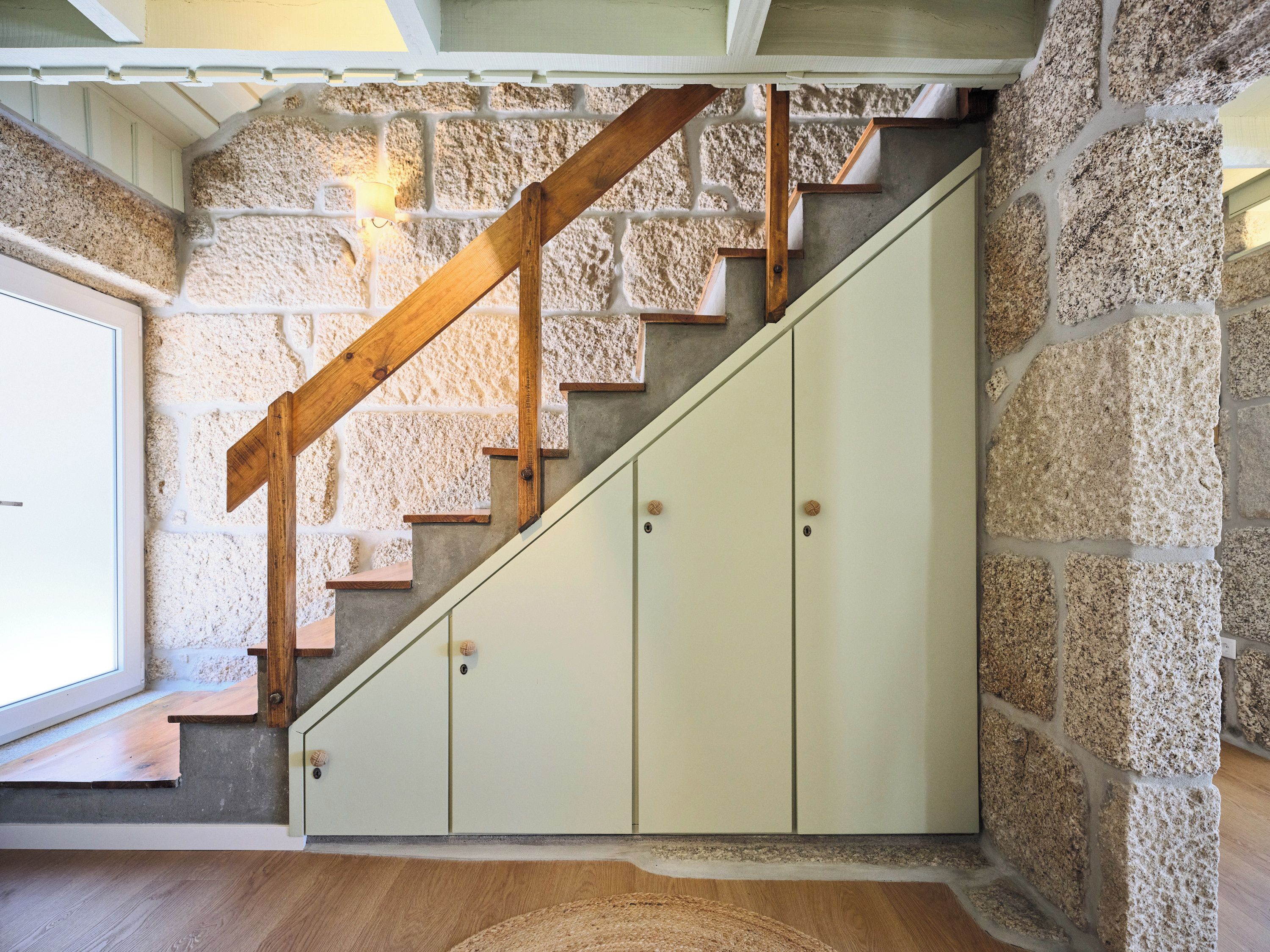 A staircase with wooden handrails and beige cabinets against a stone wall.