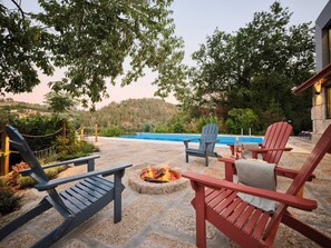Un espacio al aire libre con fogata, sillas y vista a una piscina.