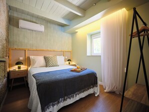 A bedroom with a bed, bedside tables, an air conditioner, a window with curtains, and a wooden floor.