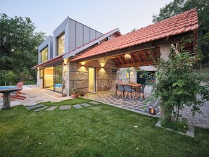 A modern house with a stone exterior, a tiled roof, and a patio with outdoor furniture. - Private Riverside Hideaway | Infinity Pool & Kayak (Maureles)