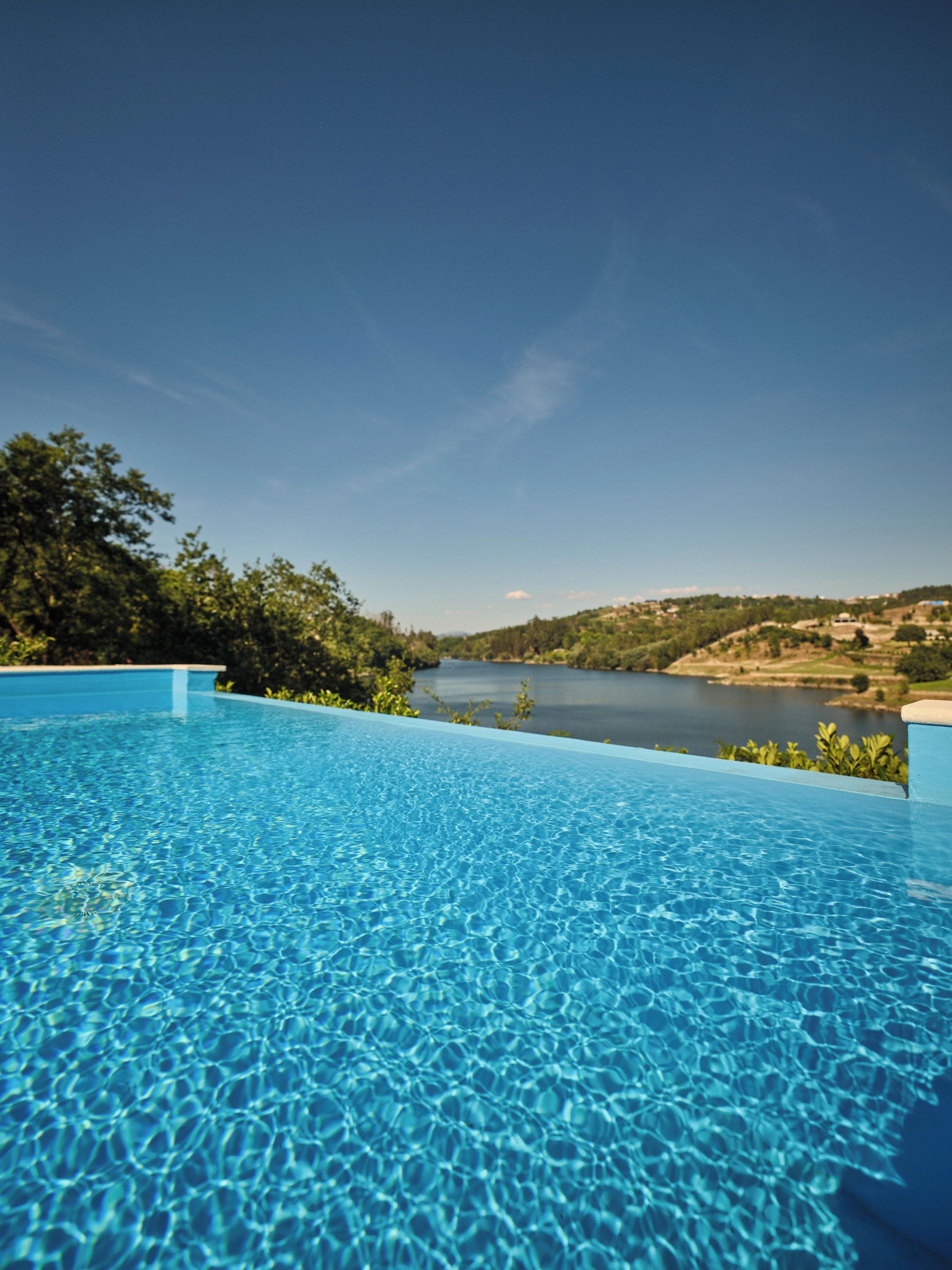 A clear blue swimming pool with a view of a lake and hills in the background.