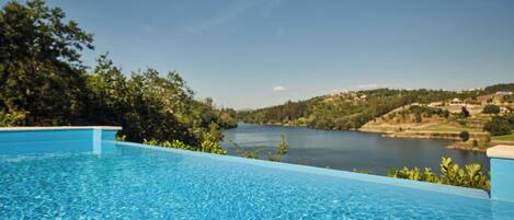 A clear blue swimming pool with a view of a lake and hills in the background.