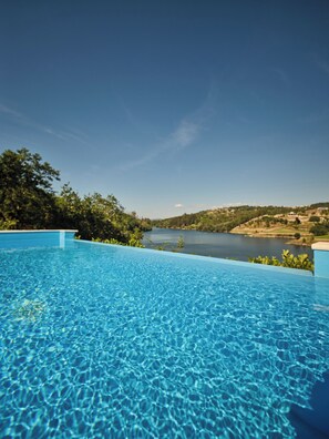Une piscine d’un bleu éclatant, avec vue sur un lac et des collines en arrière-plan.