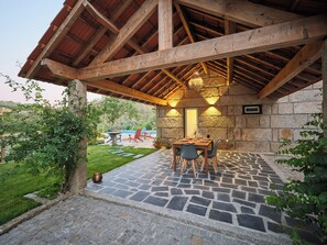 Un área de comedor al aire libre techada con suelo de piedra, vigas de madera y pared de piedra.