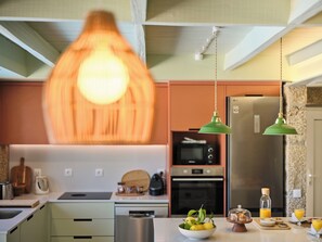 A modern kitchen with a hanging light fixture, stainless steel appliances, and a breakfast setup on the counter.
