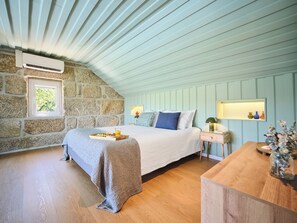 A bedroom with a stone wall, a sloped ceiling, a bed with a tray of fruit, a bedside table, and a nightstand. - Private Riverside Hideaway | Infinity Pool & Kayak (Maureles)