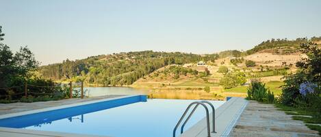Piscina con sillones de descanso y una toalla, con vista a un lago y un paisaje montañoso.
