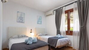 A room with two beds, a window with curtains, an air conditioning unit, and artwork on the walls. - Family villa with private pool, 500 m from the beach (Alcúdia)