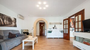 A living room with a sofa, coffee table, and a TV on a cabinet. There is a kitchen area with cabinets and a door leading to another room. - Family villa with private pool, 500 m from the beach (Alcúdia)