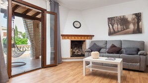 A living room with a grey sofa, a white coffee table, a fireplace, and a large window with a view of greenery. - Family villa with private pool, 500 m from the beach (Alcúdia)