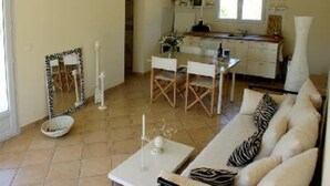 A living room with a sofa, a dining table, and chairs. There is a kitchen area with cabinets and a window. - House / Villa - Coustouge (Coustouge)