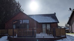 Lumihangen ympäröimä puinen mökki, jossa on terassi.
