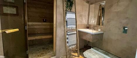 Una habitación con puerta de madera, un tapete azul, un banco de piedra, un lavabo y un espejo.