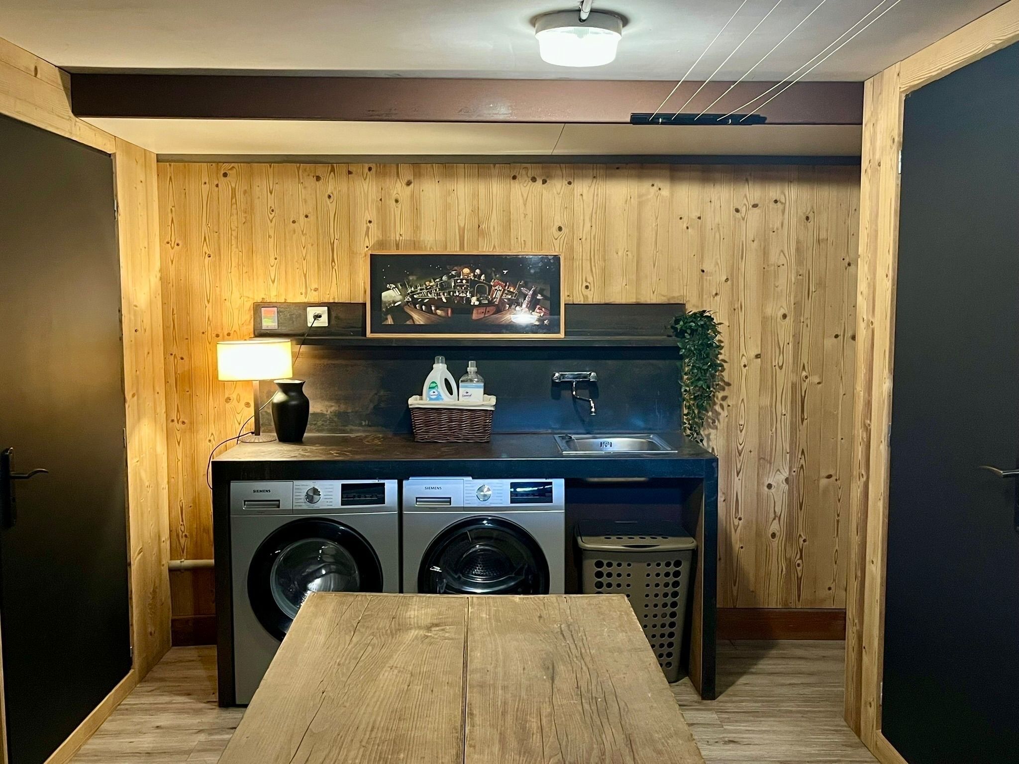 Eine kleine Küche mit Holzvertäfelung, einer Waschmaschine, einem Spülbecken, einem Tisch und einem gerahmten Bild an der Wand.