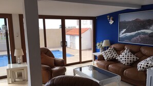 Un salon avec un canapé en cuir marron, une table basse en verre et une vue sur une piscine, visible à travers des portes vitrées.
