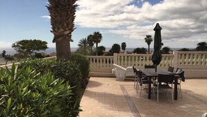 Une terrasse extérieure avec une table et des chaises, entourée de verdure et offrant une vue sur la mer.