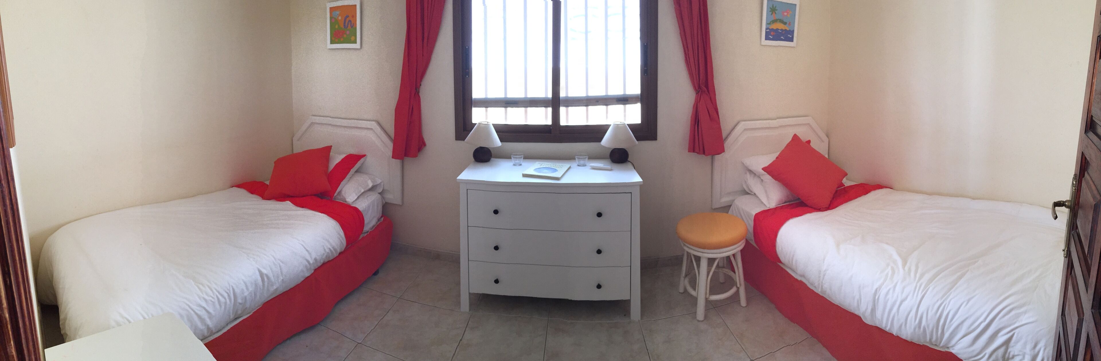 Una habitación pequeña y limpia con dos camas individuales, un escritorio pequeño con una silla y una ventana con cortinas.