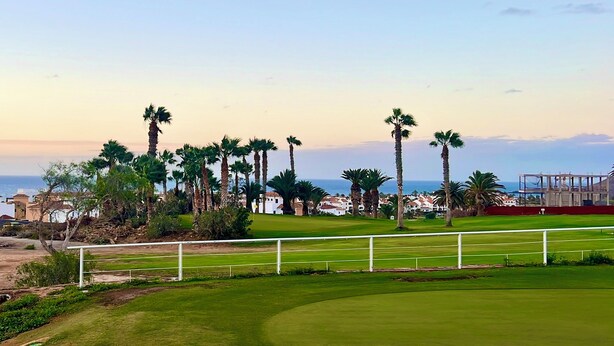 Un parcours de golf offrant une vue dégagée sur l’océan et les palmiers.