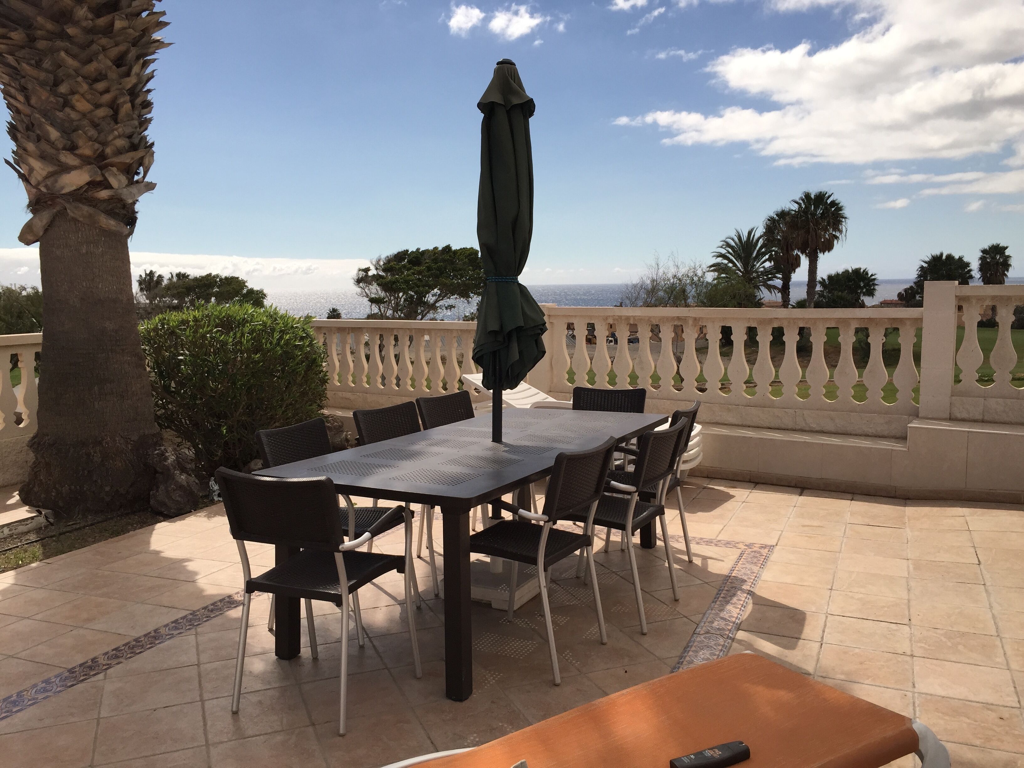 Een buitenterras met een tafel, stoelen, een parasol en uitzicht op zee.