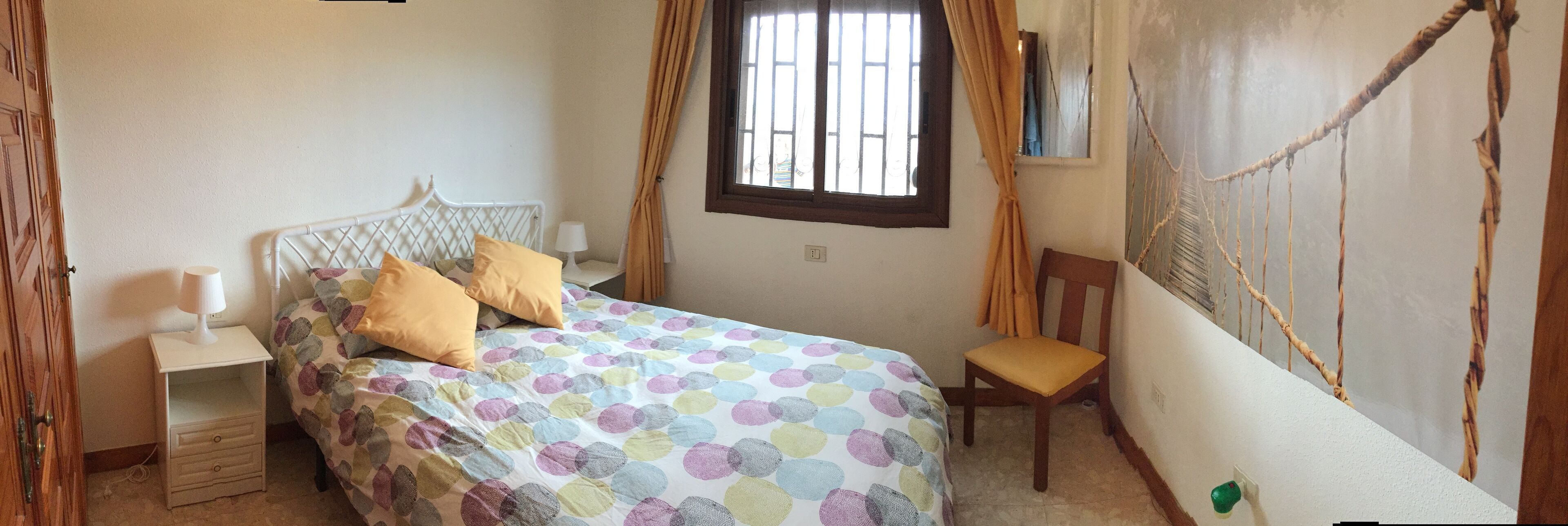 A bedroom with a bed, bedside table, chair, window, and wall decorations.