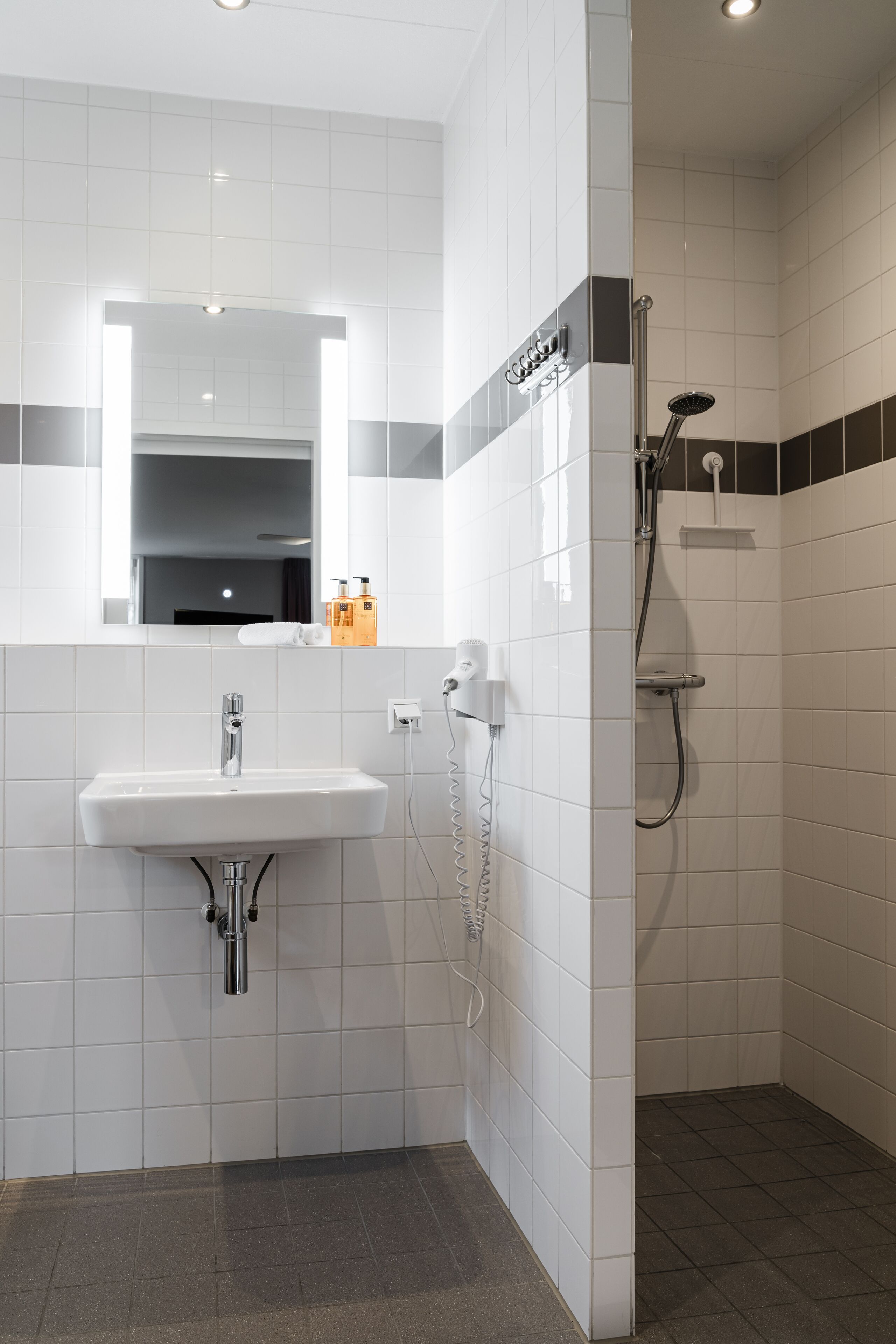 A modern bathroom with a white sink, a mirror, and a shower area.