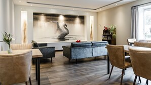 Uma sala de estar moderna com uma grande obra de arte pendurada na parede retratando cisnes, um sofá, uma mesa de centro e um espaço de jantar com cadeiras.