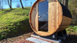 A wooden barrel-shaped structure with a door, set on a concrete base with a stone pathway leading to it. - WesterOurthe 6 persons with sauna (Durbuy)