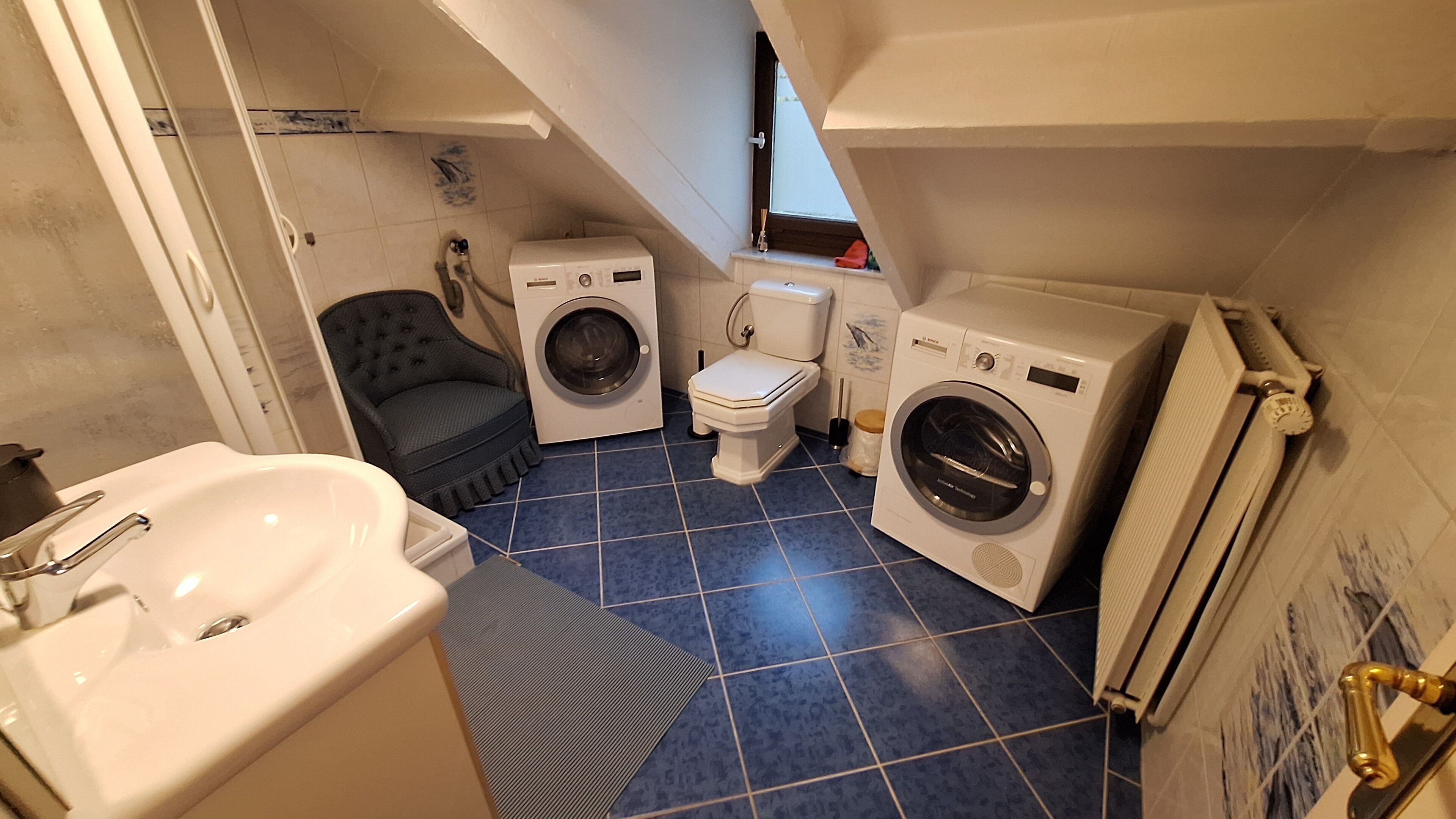 Une petite salle de bain compacte, équipée d’un lavabo, de deux machines à laver, de toilettes et d’un radiateur.