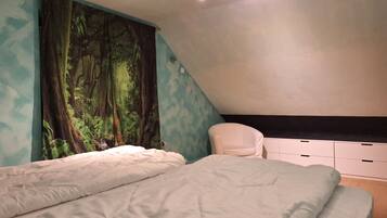 A bedroom with a large forest mural, a white bed, a white chair, and a built-in bench with storage drawers.