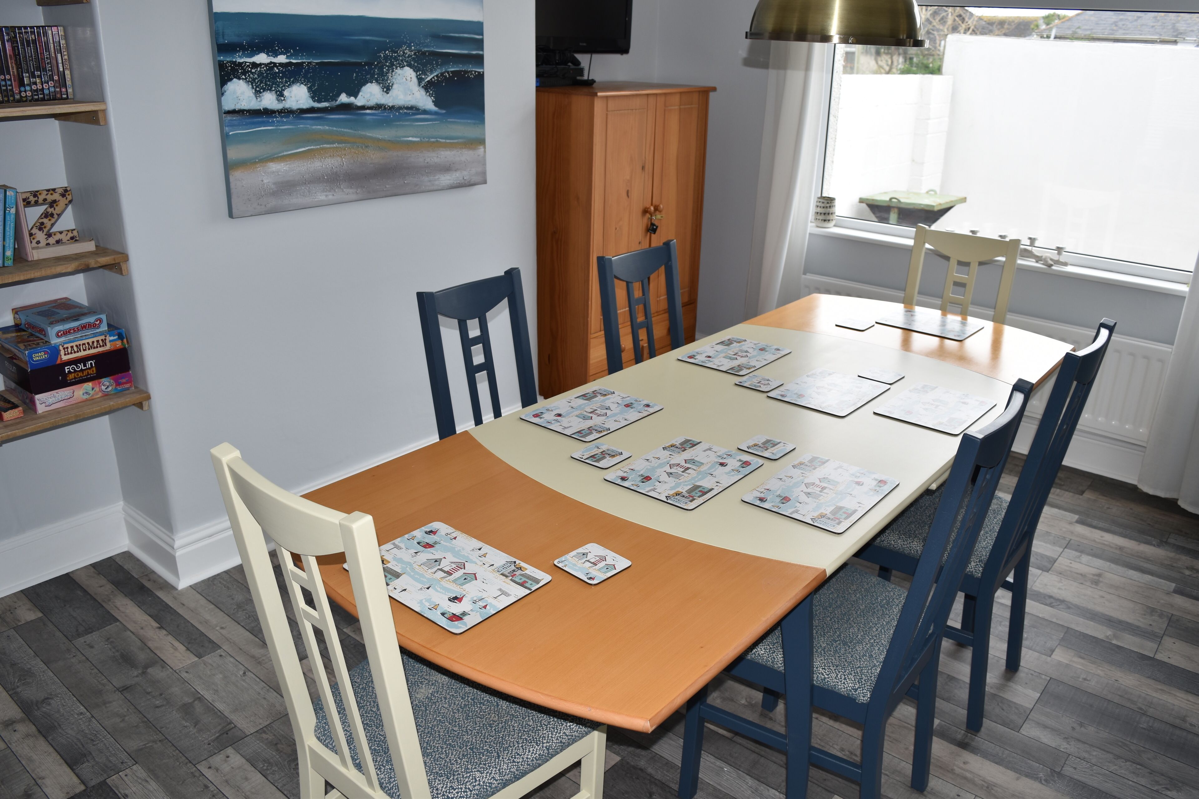 Een eetruimte met een houten tafel, blauwe stoelen en een schilderij van een strand.