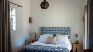 Un dormitorio con colcha estampada, cabecera azul y blanca, dos mesitas de noche con lámparas y una lámpara colgante.