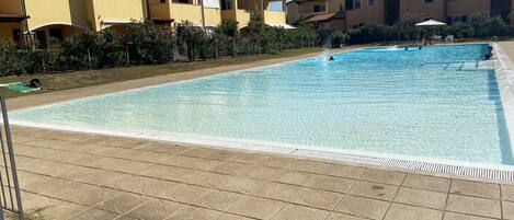 En swimmingpool med flisegulv, omgivet af bygninger med altaner og en klar himmel.