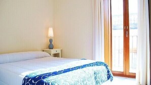 A hotel room with a bed, a nightstand with a lamp, and a sliding glass door to the outside.