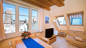 A cozy living room with a large window, a wooden dining table, a TV, and a patterned armchair. - Comfortable apartment in the heart of Gdansk Old Town (Gdansk)