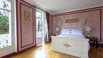 Une chambre avec un grand lit, un plancher en bois et une vue sur l’extérieur, grâce à une porte ouverte.